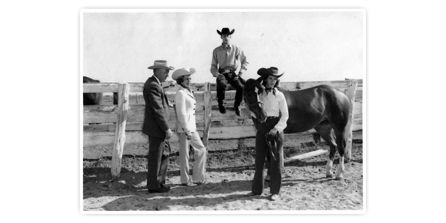 The Justin Family is posing on a fence, and daughter, Mary Justin, is holding the lead rope to a horse. 